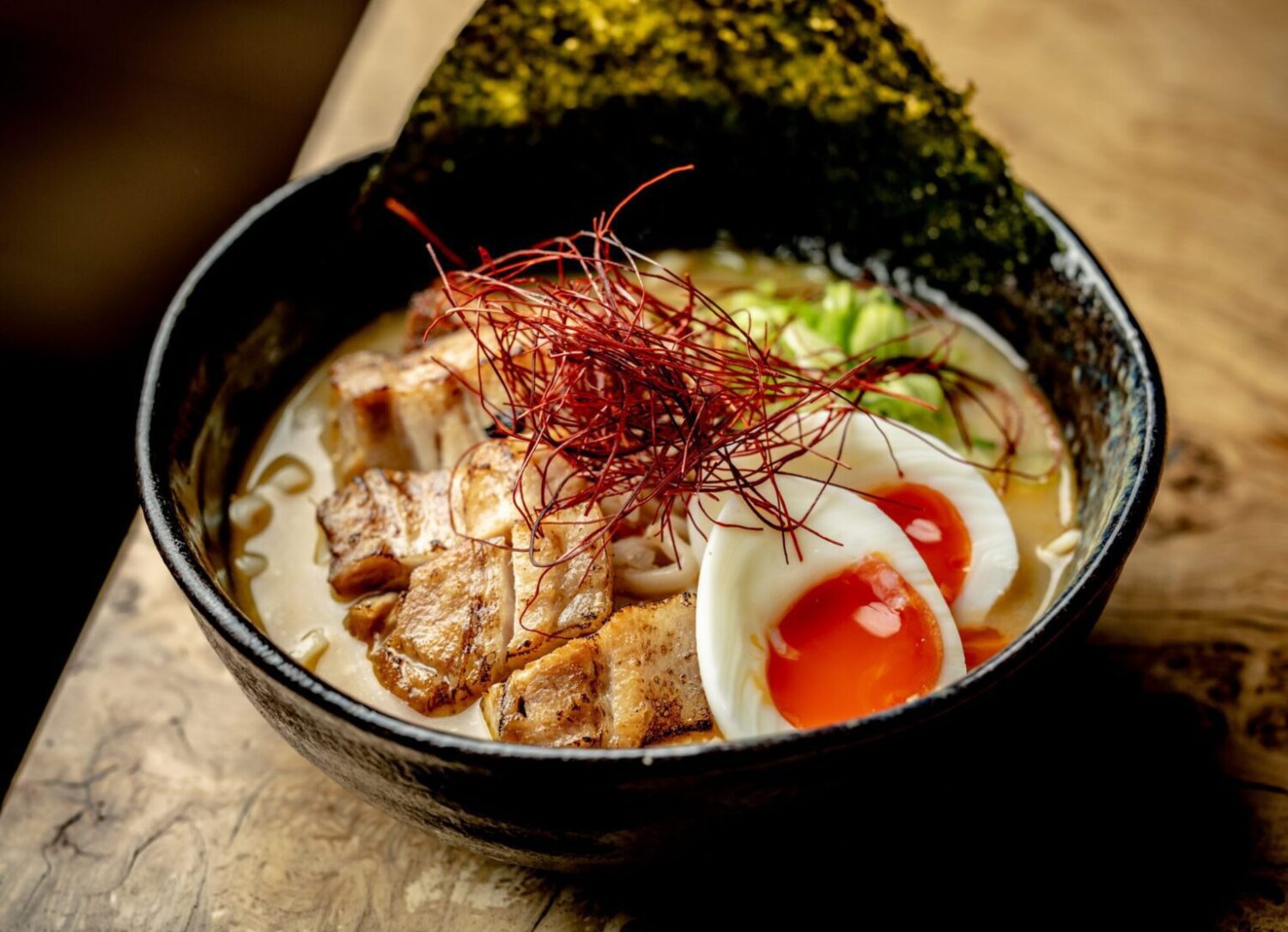 Delicious bowl of ramen topped with sliced pork, half-boiled egg, seaweed, and red pepper threads